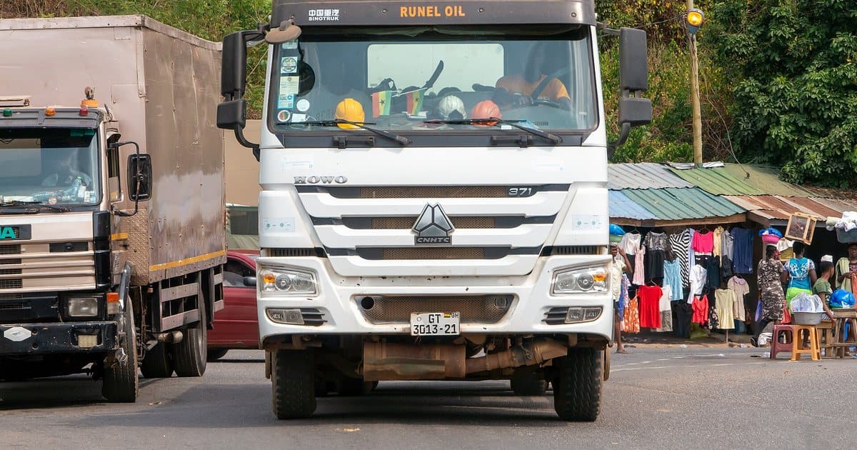 A Chinese Sinotruk HOWO truck next to an old European truck on a road in Ghana